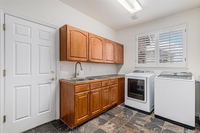 laundry room featuring washing machine and clothes dryer, visible vents, stone finish floor, cabinet space, and a sink