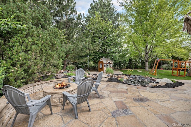 view of patio featuring a storage unit, a playground, an outbuilding, and an outdoor fire pit