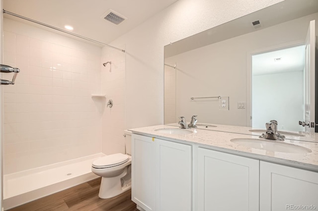 bathroom with a tile shower, double vanity, toilet, and wood finished floors