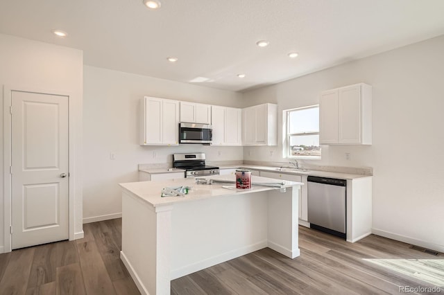 kitchen with appliances with stainless steel finishes, a center island, light wood-style floors, white cabinets, and recessed lighting