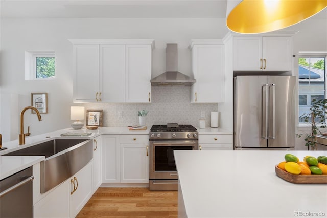 2571 S Cherokee St, Denver, CO 80223 - kitchen featuring appliances with stainless steel finishes, wall chimney exhaust hood, light wood-style floors, light countertops, and white cabinetry