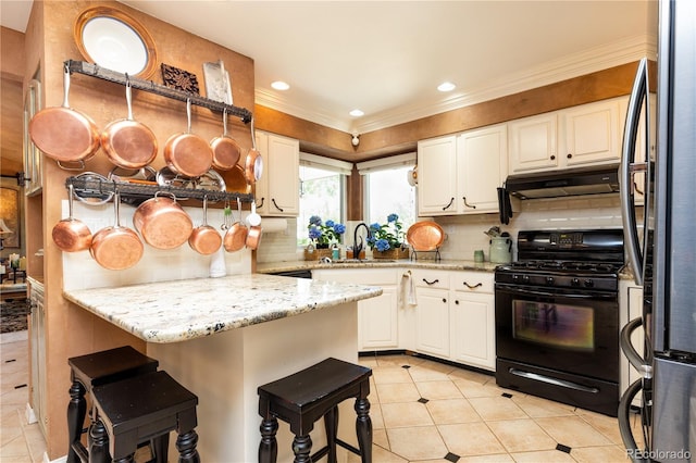 5298 Pony Creek Cir, Colorado Springs, CO 80919 - kitchen featuring black range with gas stovetop, freestanding refrigerator, under cabinet range hood, light tile patterned flooring, and white cabinets