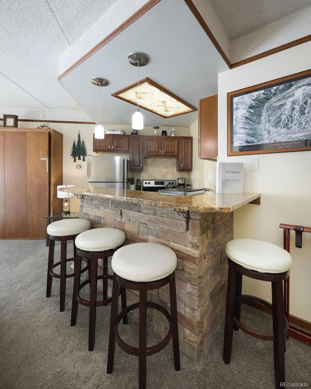 kitchen with backsplash, light carpet, light stone counters, hanging light fixtures, and stainless steel appliances