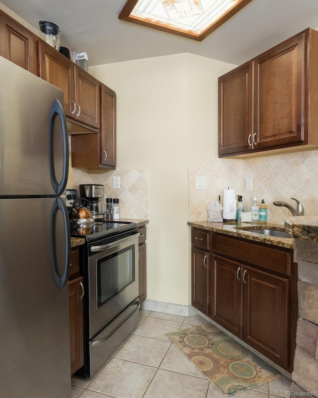 kitchen featuring light tile patterned floors, stone counters, a sink, stainless steel appliances, and backsplash