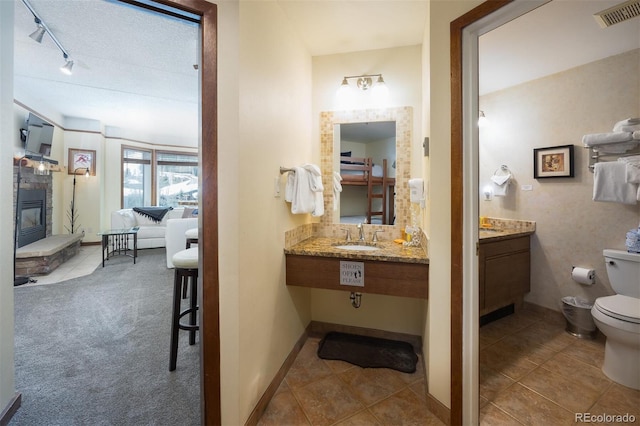 bathroom featuring visible vents, baseboards, toilet, a fireplace, and a sink