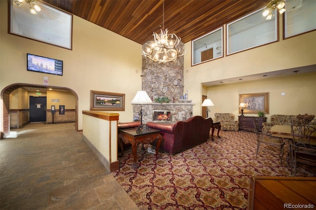 living area featuring a fireplace, arched walkways, stone finish floor, wood ceiling, and a towering ceiling