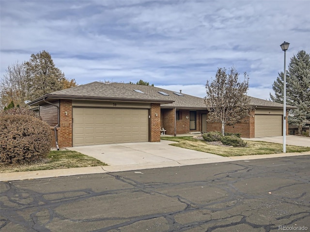 ranch-style house featuring concrete driveway, a garage, brick siding, and a shingled roof