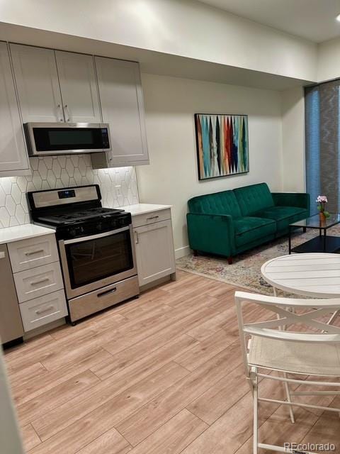 2876 W 53rd Ave Unit 305, Denver, CO 80221 - kitchen with appliances with stainless steel finishes, gray cabinetry, light countertops, light wood-style flooring, and backsplash