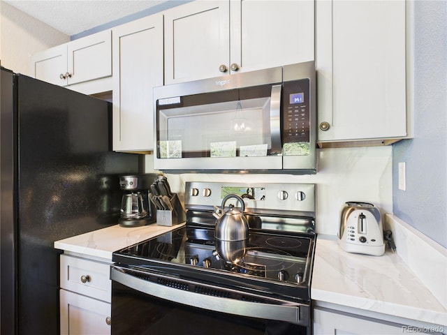 27 Lake Ridge Cir Unit 1842, Dillon, CO 80435 - kitchen with electric range, stainless steel microwave, freestanding refrigerator, white cabinetry, and light stone counters