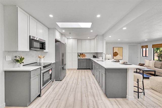 kitchen featuring appliances with stainless steel finishes, a skylight, kitchen peninsula, gray cabinetry, and a breakfast bar area