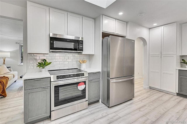 kitchen featuring light wood-type flooring, backsplash, gray cabinetry, and stainless steel appliances