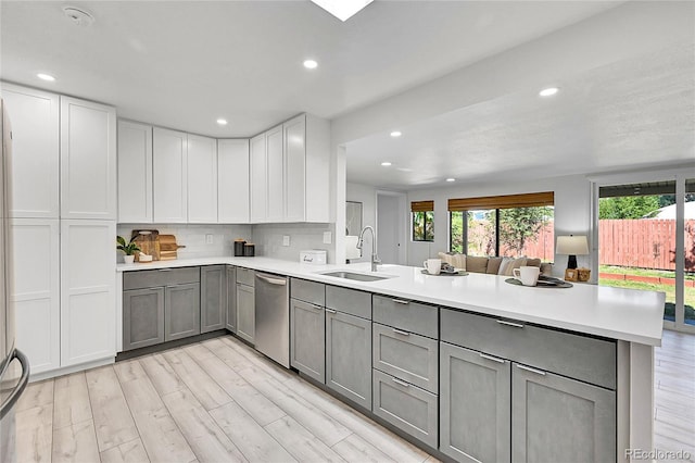 kitchen with kitchen peninsula, dishwasher, sink, backsplash, and gray cabinetry