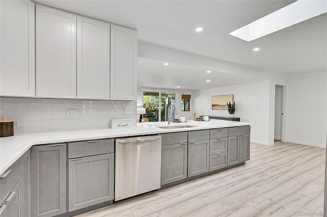 kitchen with dishwasher, a skylight, tasteful backsplash, sink, and gray cabinets