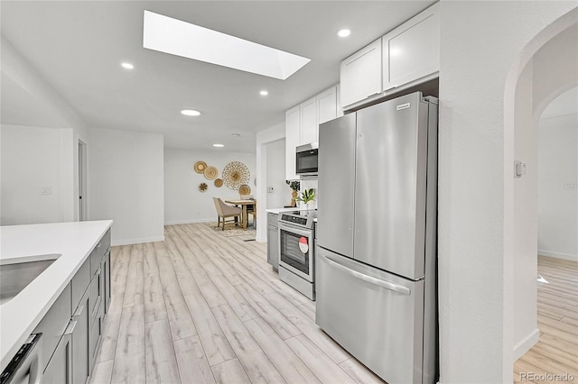 kitchen with light hardwood / wood-style floors, white cabinetry, appliances with stainless steel finishes, and a skylight