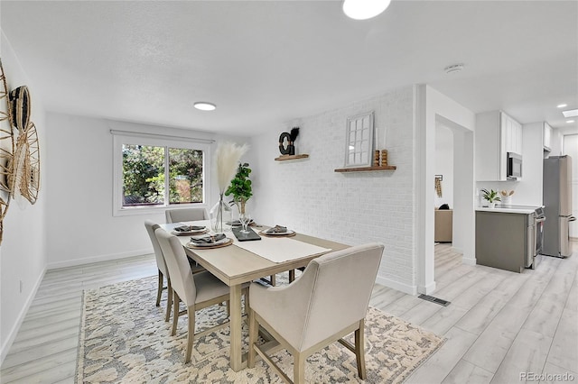 dining area featuring light wood-type flooring and brick wall