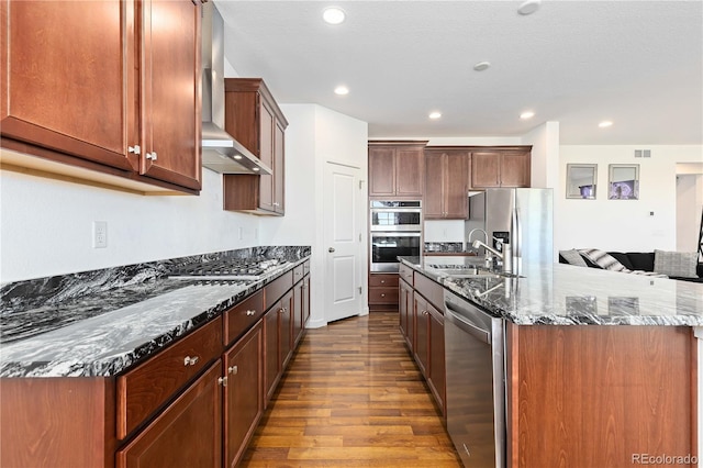 kitchen featuring sink, wood-type flooring, wall chimney range hood, stainless steel appliances, and dark stone countertops