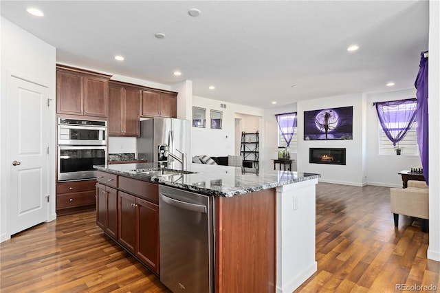 kitchen featuring an island with sink, light stone counters, appliances with stainless steel finishes, and dark hardwood / wood-style flooring