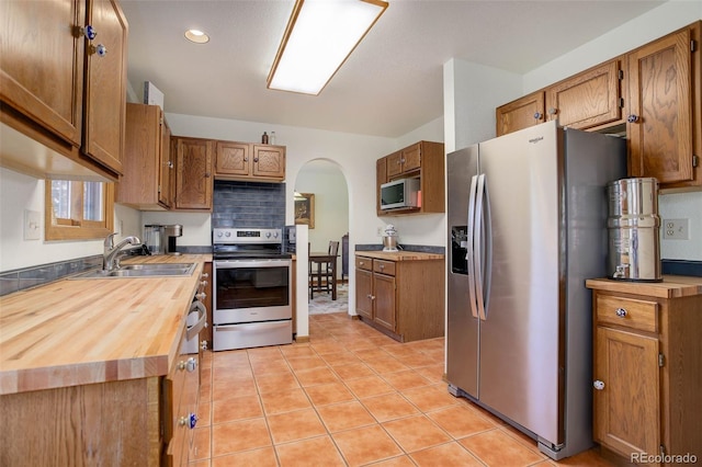 kitchen featuring sink, tasteful backsplash, wooden counters, light tile patterned floors, and appliances with stainless steel finishes