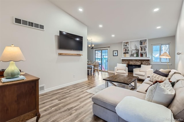 living room with an inviting chandelier, hardwood / wood-style floors, a stone fireplace, and a healthy amount of sunlight