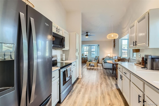 kitchen with light hardwood / wood-style flooring, white cabinetry, hanging light fixtures, black fridge, and stainless steel range with electric cooktop