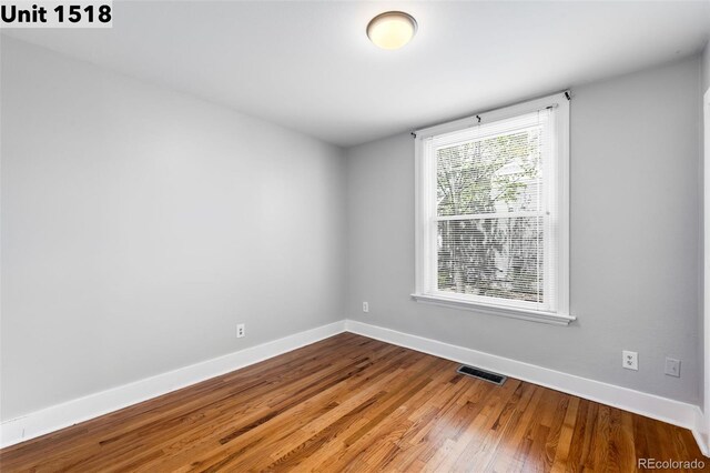 unfurnished room with baseboards, wood finished floors, and visible vents
