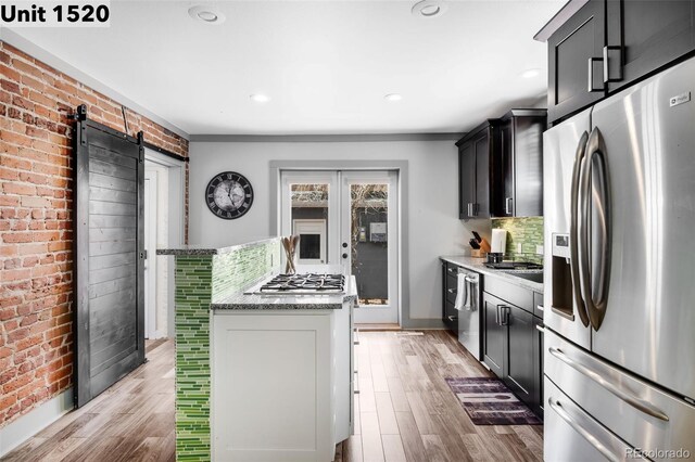 kitchen featuring decorative backsplash, light stone countertops, light wood-style floors, a barn door, and appliances with stainless steel finishes