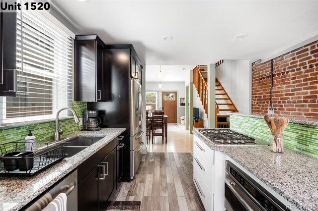 kitchen featuring light wood-style floors, a sink, appliances with stainless steel finishes, and light stone counters