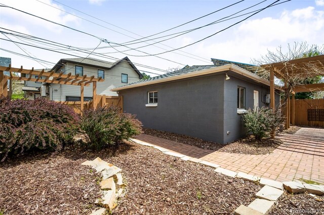 view of property exterior featuring fence, a pergola, and concrete block siding