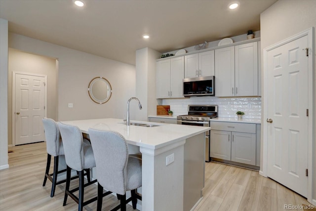 2785 Black Hawk Pl, Brighton, CO 80601 - kitchen featuring stainless steel appliances, a sink, an island with sink, backsplash, and light wood-style flooring