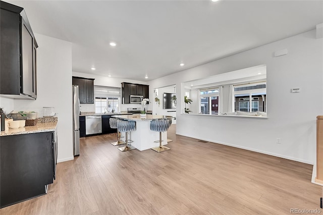 kitchen with a center island with sink, a breakfast bar, light stone countertops, light wood-type flooring, and appliances with stainless steel finishes