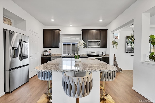 kitchen with a center island, appliances with stainless steel finishes, light hardwood / wood-style floors, and light stone counters