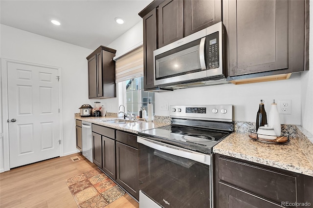 kitchen with light stone counters, appliances with stainless steel finishes, dark brown cabinetry, sink, and light hardwood / wood-style floors