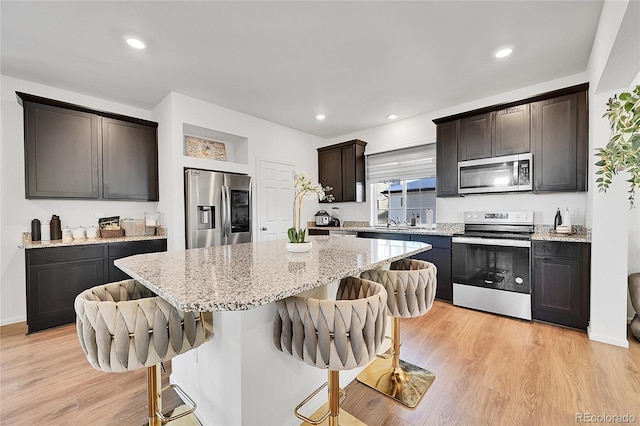 kitchen with a kitchen breakfast bar, light hardwood / wood-style flooring, appliances with stainless steel finishes, and a center island