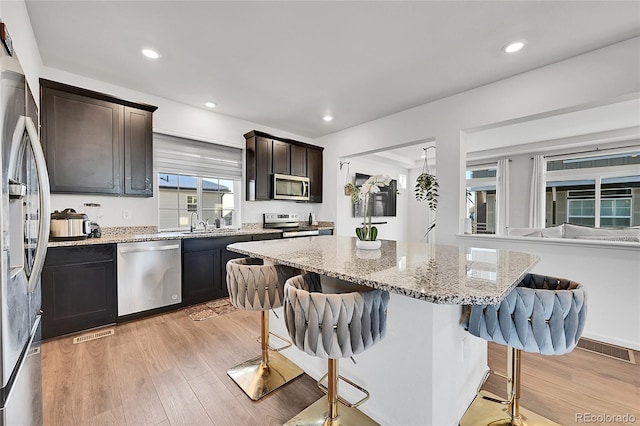 kitchen featuring stainless steel appliances, a center island, light stone counters, a kitchen breakfast bar, and light hardwood / wood-style flooring