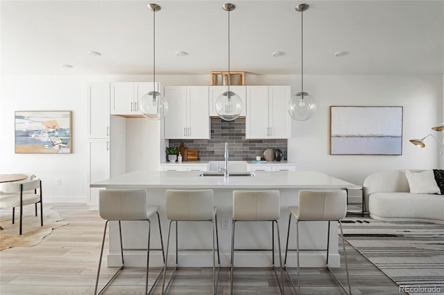 kitchen featuring tasteful backsplash, a kitchen island with sink, sink, pendant lighting, and white cabinetry