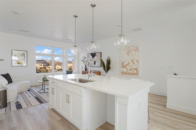 kitchen with sink, light hardwood / wood-style flooring, decorative light fixtures, a center island with sink, and white cabinets