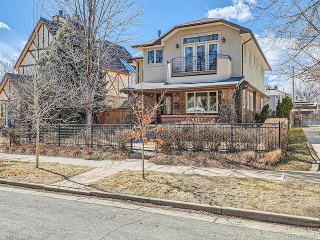 view of front of house featuring brick siding, a fenced front yard, a balcony, and stucco siding