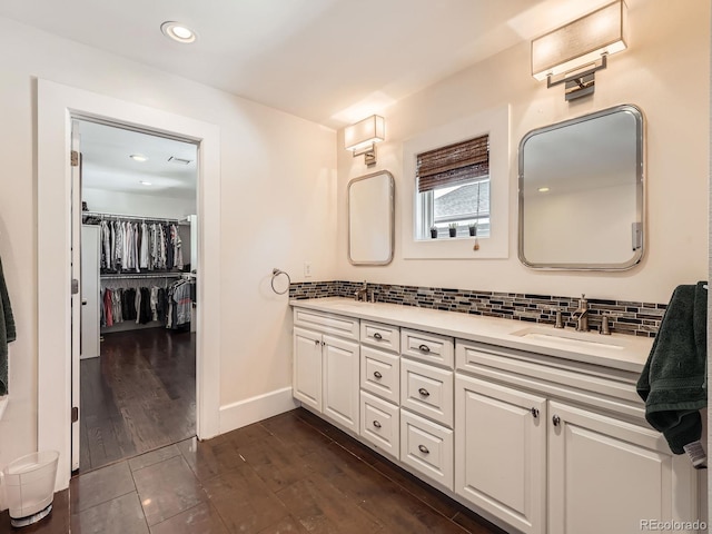 full bath featuring double vanity, baseboards, wood finished floors, a sink, and backsplash