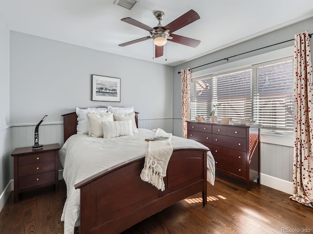 bedroom featuring dark wood-type flooring, wainscoting, ceiling fan, and visible vents