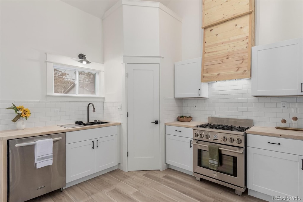 kitchen featuring white cabinets, light wood-type flooring, butcher block counters, sink, and stainless steel appliances