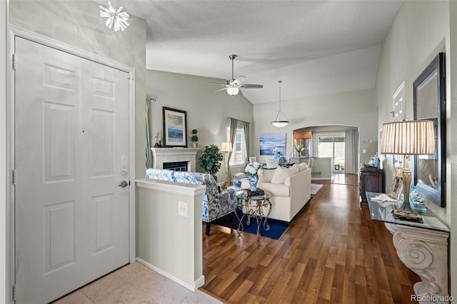 foyer entrance featuring arched walkways, a fireplace, ceiling fan, lofted ceiling, and baseboards