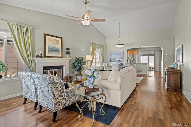 living room featuring ceiling fan, a tile fireplace, wood finished floors, high vaulted ceiling, and baseboards