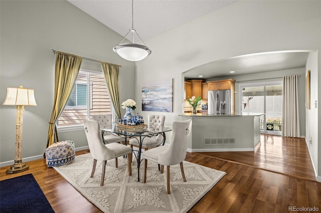 dining room with plenty of natural light, arched walkways, wood finished floors, baseboards, and high vaulted ceiling