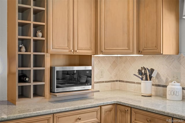 kitchen with stainless steel microwave, light stone counters, and tasteful backsplash