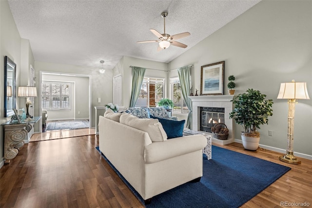 living room featuring a textured ceiling, a ceiling fan, wood finished floors, a fireplace, and baseboards