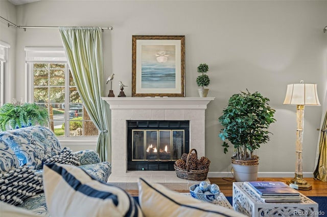 living area featuring a tiled fireplace, wood finished floors, and baseboards