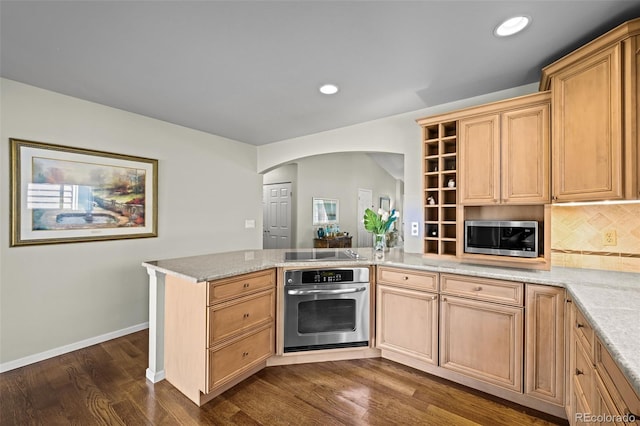 kitchen with appliances with stainless steel finishes, arched walkways, a peninsula, dark wood-style floors, and tasteful backsplash