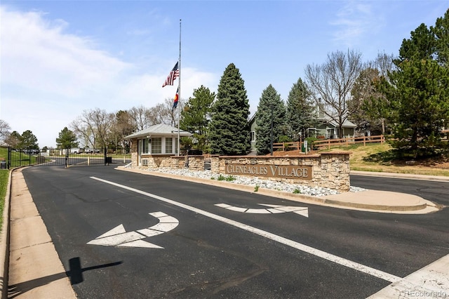 view of asphalt road with curbs, a gate, and a gated entry