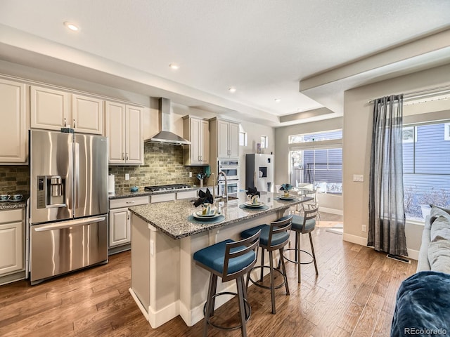 kitchen with stainless steel appliances, a breakfast bar area, wall chimney exhaust hood, and wood finished floors