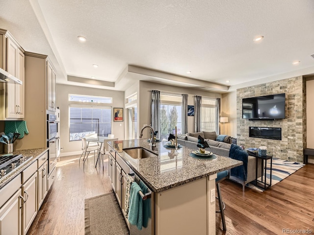 kitchen with a breakfast bar, a center island with sink, wood-type flooring, cream cabinets, and a sink